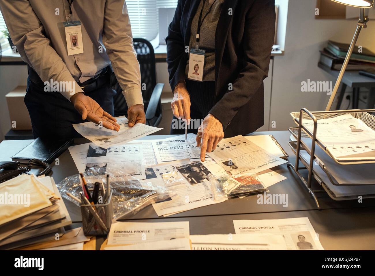 Hände interkultureller Agenten des FBI, die kriminelle Profile am Arbeitsplatz diskutieren, während einer von ihnen auf das Foto des Verdächtigen zeigt Stockfoto