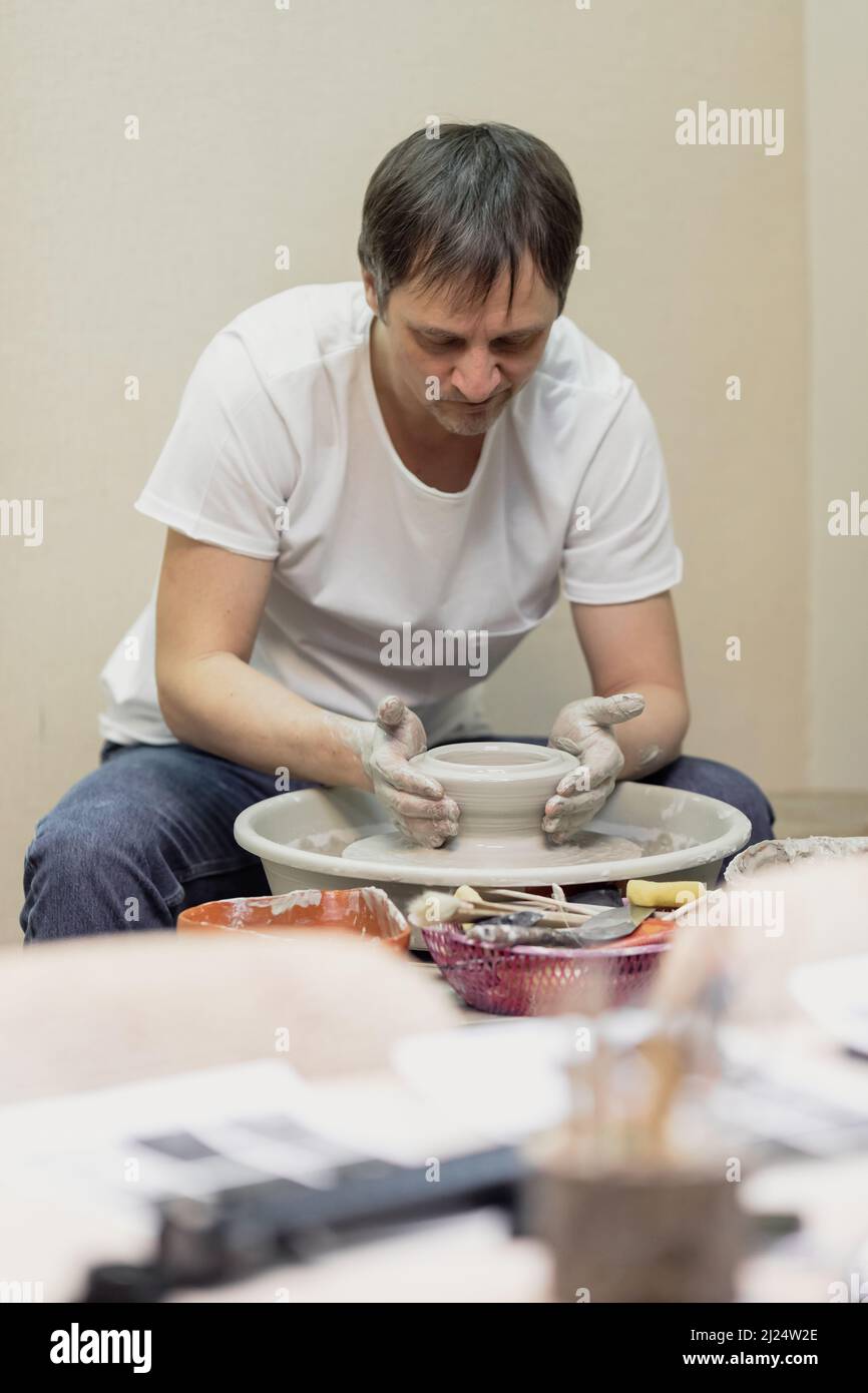 Ein Mann in einem weißen T-Shirt und Jeans, in einer Töpferwerkstatt, der hinter einem Töpferrad arbeitet Stockfoto