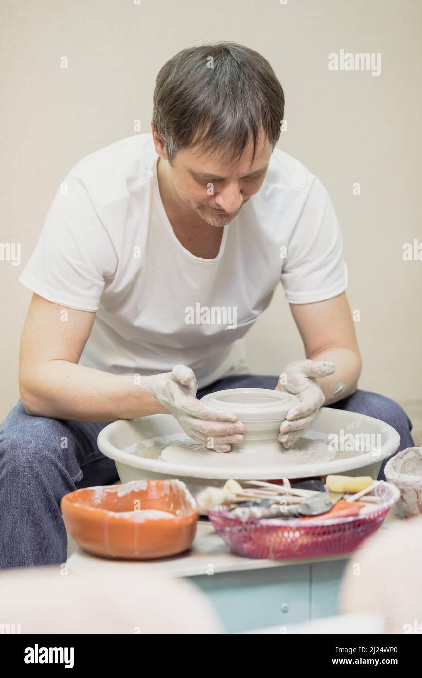 Ein Mann in einem weißen T-Shirt und Jeans, in einer Töpferwerkstatt, der hinter einem Töpferrad arbeitet Stockfoto