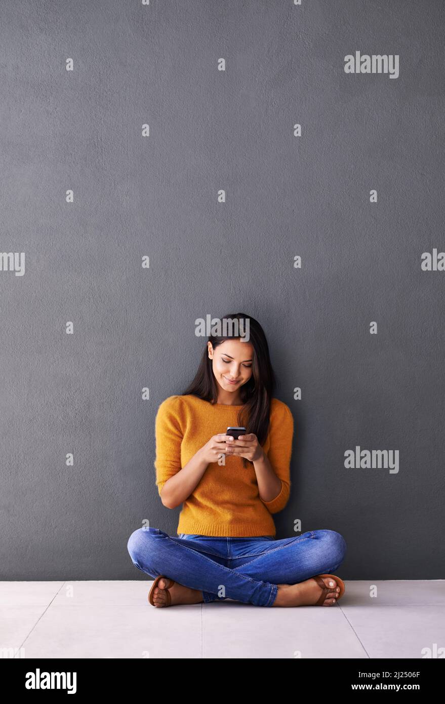 Etwas Liebe in die Welt hinaus senden. Aufnahme einer attraktiven jungen Frau, die ein Mobiltelefon benutzt, während sie auf dem Boden sitzt. Stockfoto