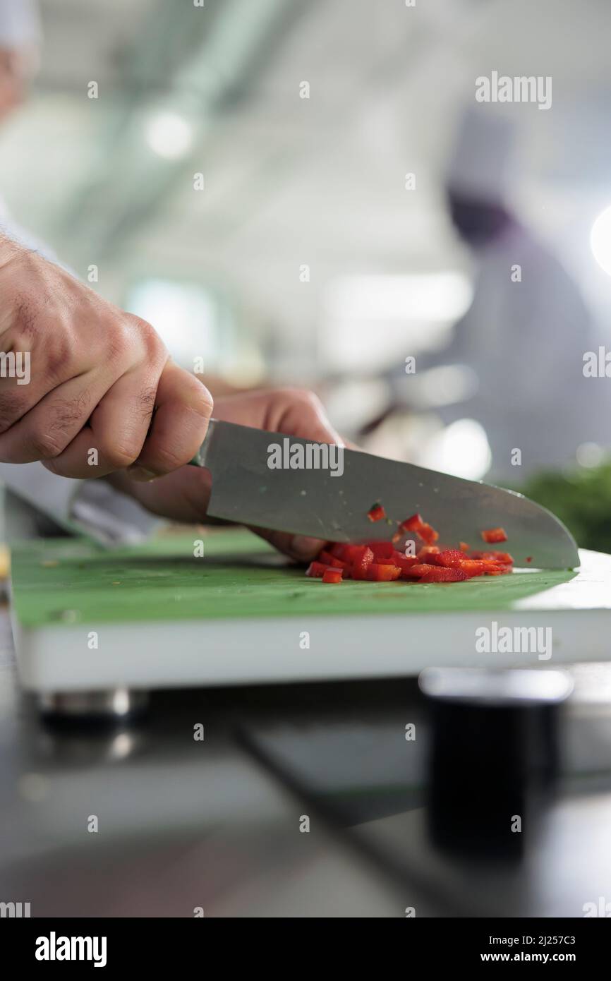 Nahaufnahme der Hände des Chefkochs, die frischen und biologischen roten Paprika schneiden, während sie Gourmet-Gerichte zum Abendessen zubereiten. Gastronomieexperte schneidet Gemüse und Gemüse für köstliche Mahlzeiten. Stockfoto