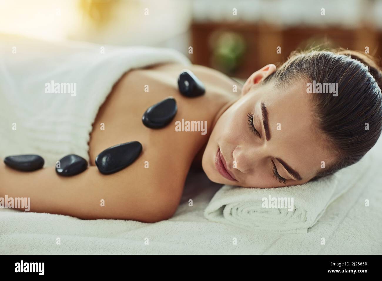 Förderung der Muskelentspannung mit heißen Steinen. Aufnahme einer attraktiven jungen Frau, die in einem Beauty Spa eine Hot Stone Massage bekommt. Stockfoto