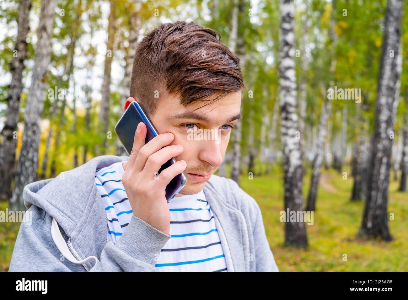 Trauriger junger Mann mit Mobiltelefon im Herbstwald Stockfoto