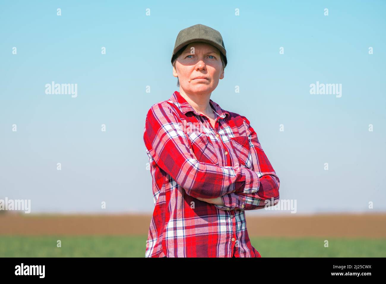 Porträt einer Bäuerin auf einem kultivierten Weizensämlingsfeld, einer Landarbeiterin mit kariertem Hemd und Baseballmütze Stockfoto