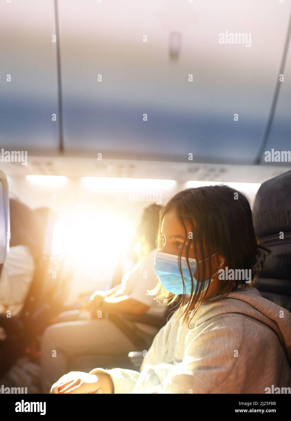 Junges Mädchen in einem Flugzeug am sonnigen Tag mit Maske im Gesicht Stockfoto