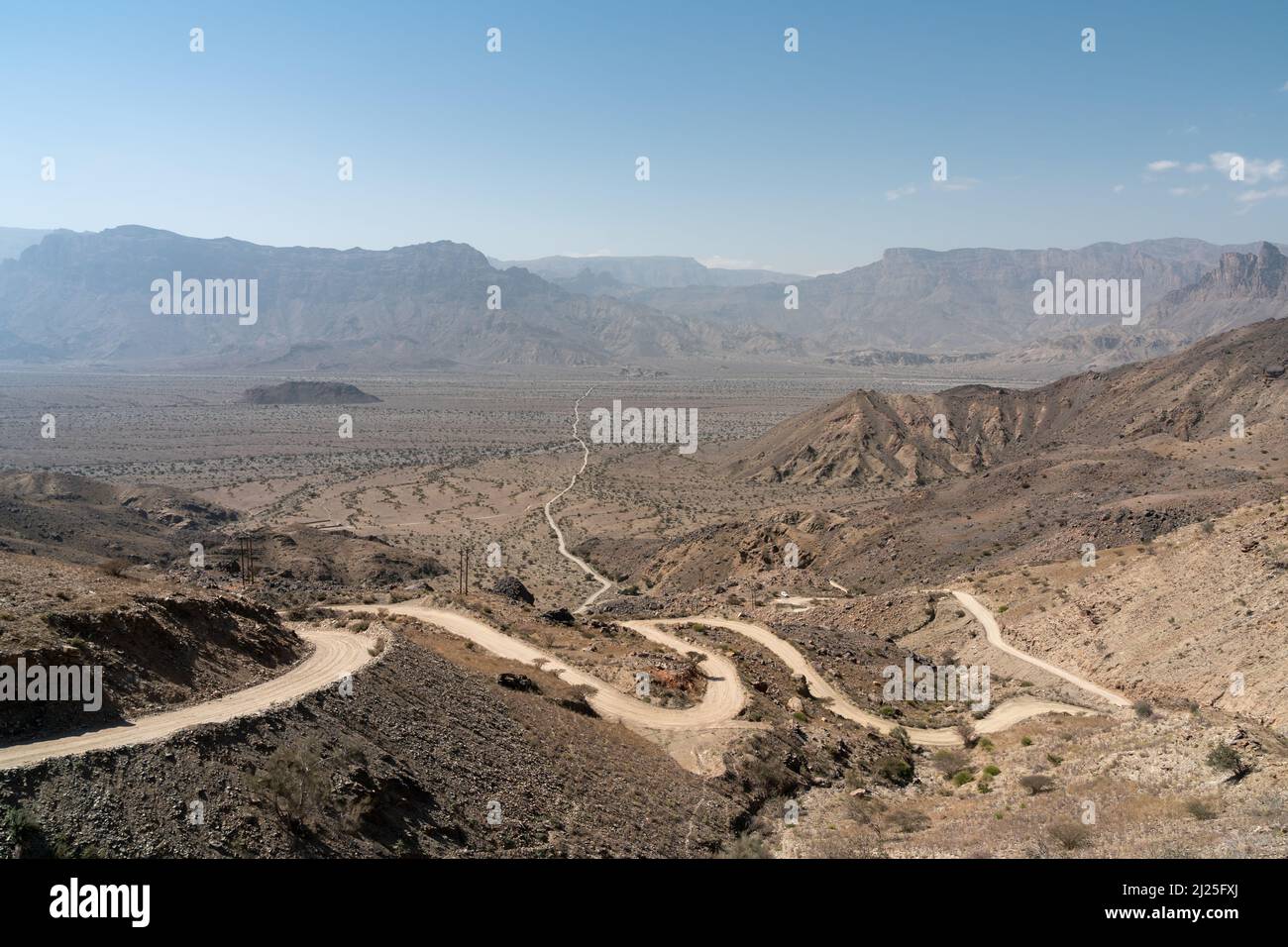 Eine kurvenreiche Schotterstraße, die einen Berg hinunter zur flachen Weite der Ghubrah Bowl führt, umgeben von den kargen östlichen Bergen des hascharen Ostens im Oman Stockfoto