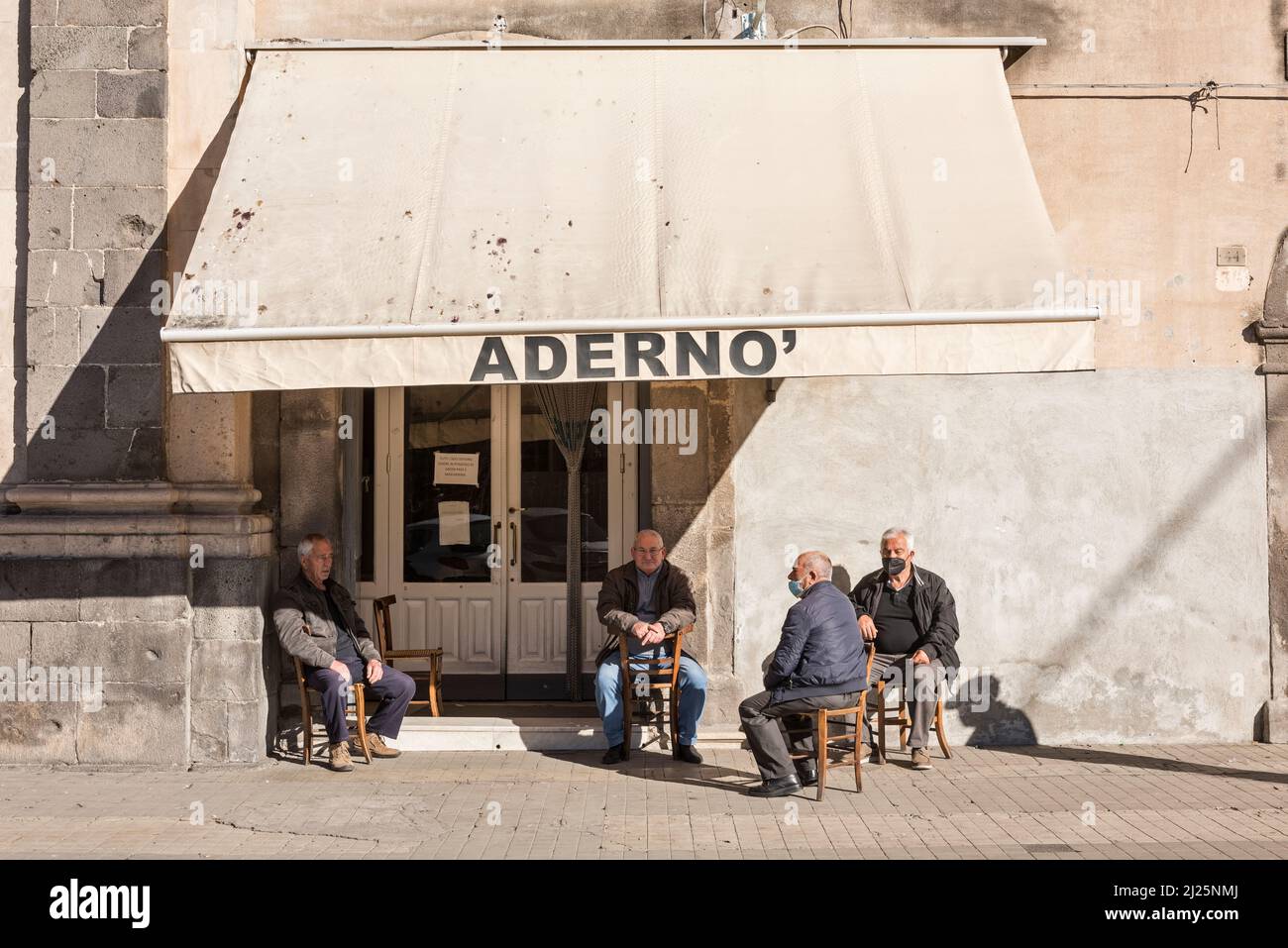 Ältere Männer sitzen in der Sonne in ihrem Club vor dem Monastero di Santa Lucia in Adrano, Sizilien, Italien, gegründet 1157 als Benediktinerkloster Stockfoto