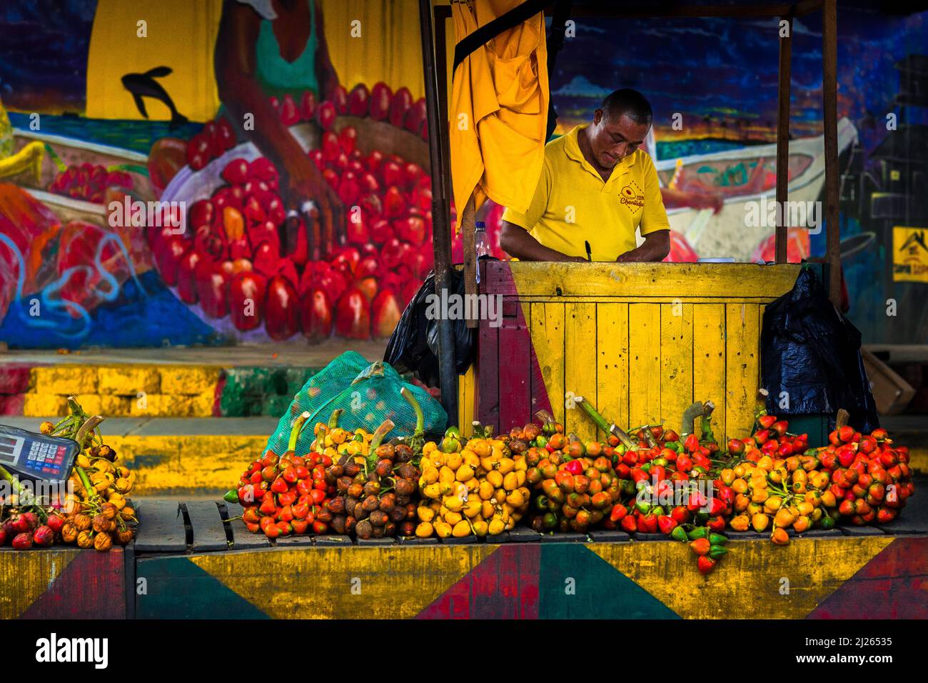 Ein afro-kolumbianischer Straßenhändler verkauft rohe Früchte der Pfirsichpalme unter der Autobahnbrücke in Cali, Valle del Cauca, Kolumbien. Stockfoto