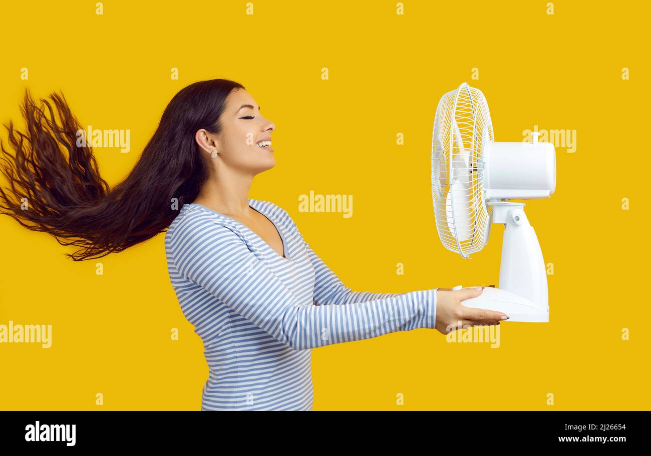 Seitenansicht einer glücklichen Frau, die einen elektrischen Ventilator hält und die frische Luft in ihr Gesicht bläst Stockfoto
