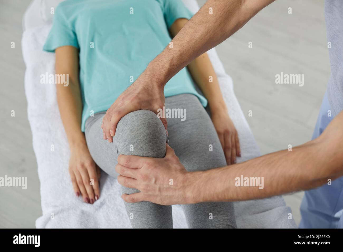 Der männliche Therapeut massiert das Knie der Patientin während der Physiotherapie im Krankenhaus. Stockfoto