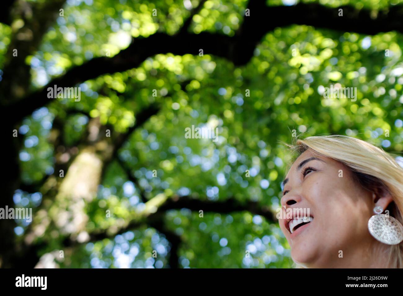 Lächelnder fröhlicher Frauenheld unter einem grünen Baum. Konzept des Glücks. Stockfoto