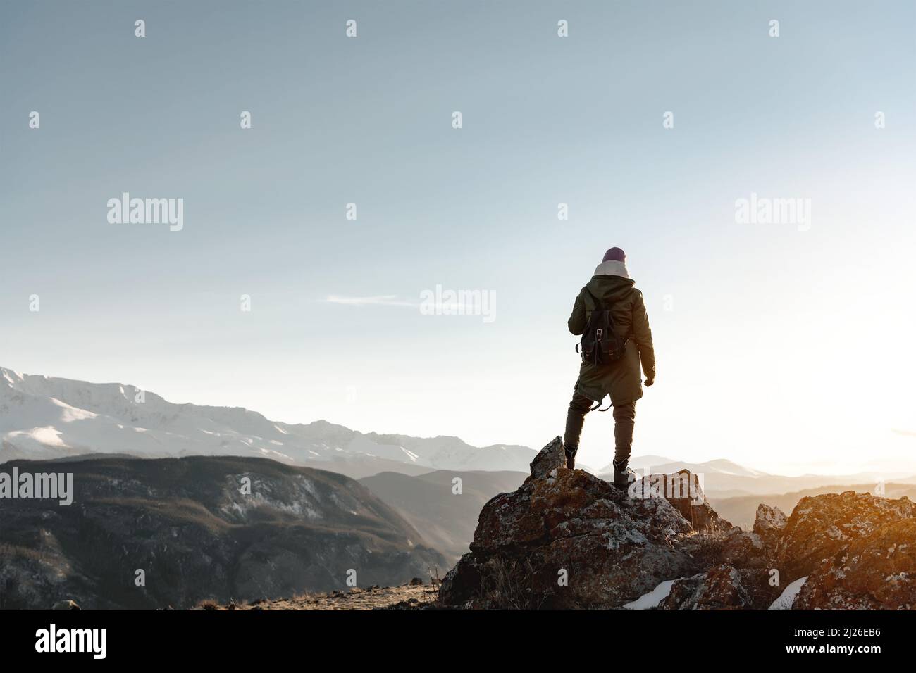 Die junge Wanderin steht auf einem großen Felsen vor der Kulisse der Berge und beobachtet den Sonnenuntergang Stockfoto