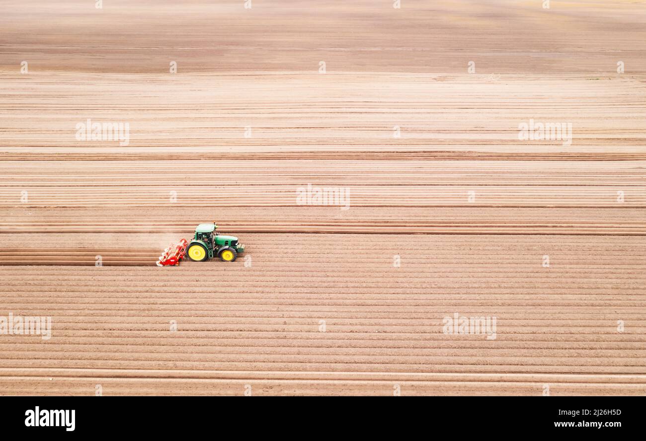 Einsamer Traktor auf landwirtschaftlichem Feld mit Reihen von gepflügten Böden. Landwirtschaftliche Felder für die Anpflanzung von Pflanzen vorbereitet, Ansicht von oben. Konzept der industriellen Landwirtschaft. Drohnenfotografie Stockfoto
