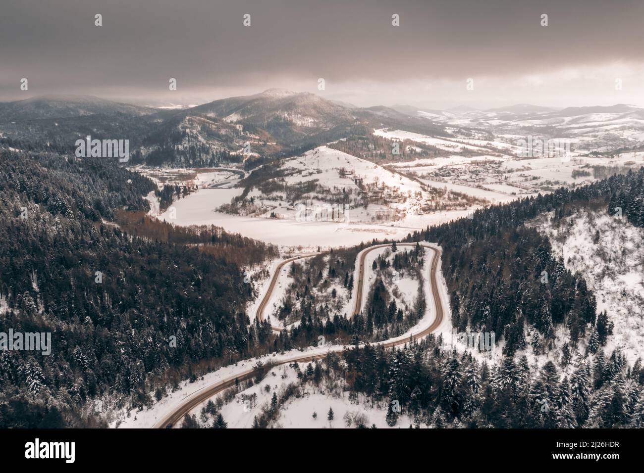 Luftdrohne Blick über die Winterberge mit Bergstraße Serpentin, Fluss und Wald. Landschaftsfotografie Stockfoto