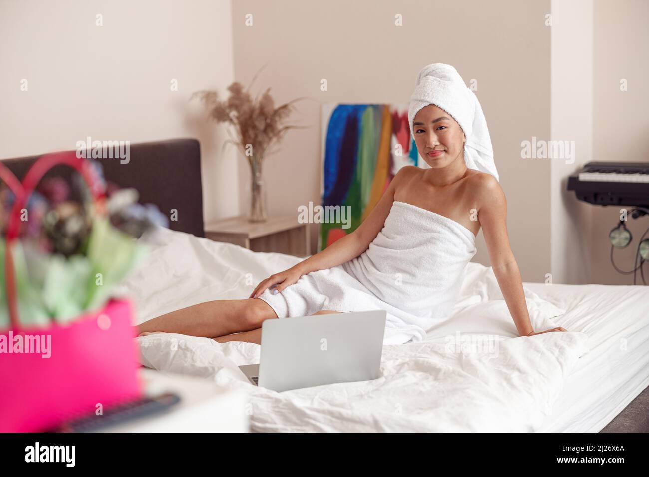 Lächelnde junge Frau, die zu Hause mit einem Laptop auf dem Bett sitzt Stockfoto