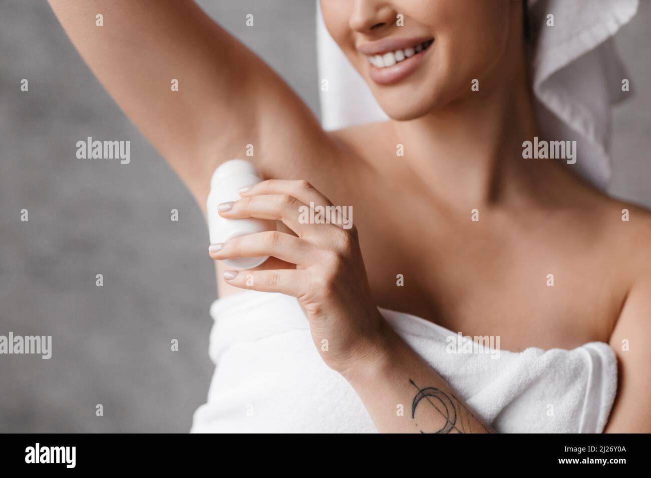 Fröhliche kaukasische Dame, die Rollo-Deodorant auf die Achselhöhle anwendet, während sie im Badezimmer tägliche Schönheitsroutine macht Stockfoto