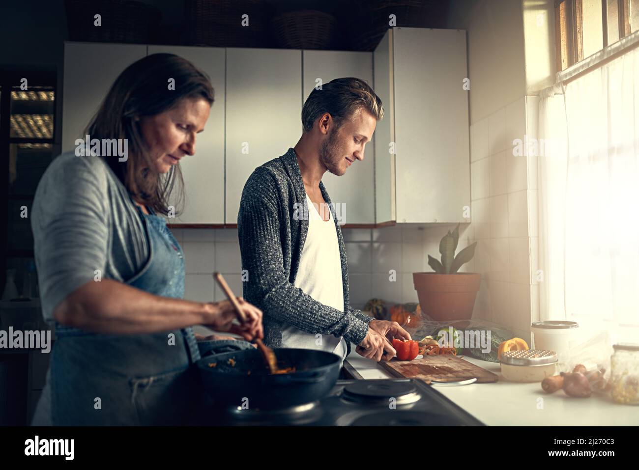 Beim Kochen mit Mama verbinden. Aufnahme einer Mutter und ihres erwachsenen Sohnes, die zu Hause in ihrer Küche kochen. Stockfoto