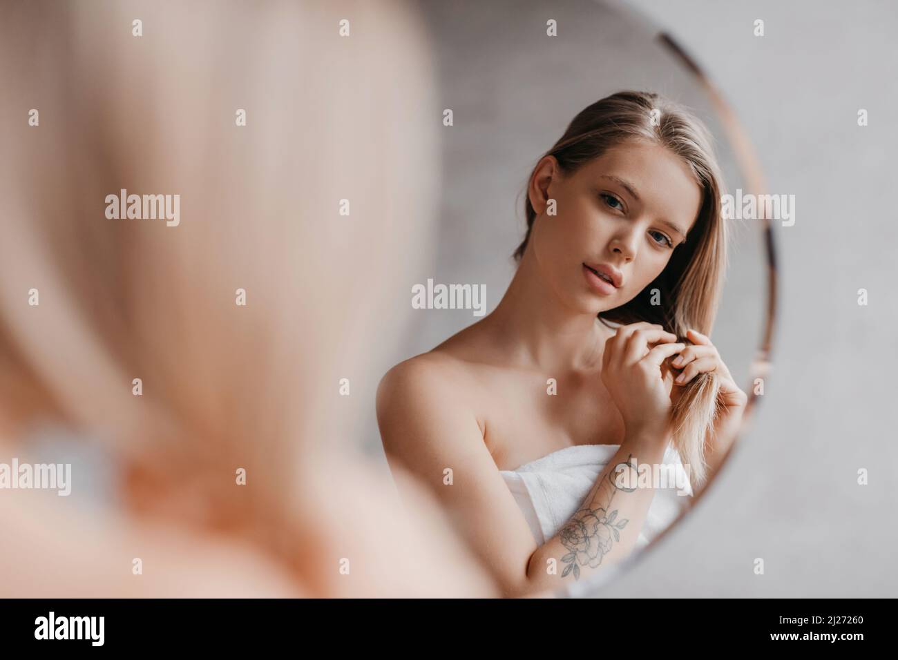 Natürliche Schönheit. Die hübsche junge Dame berührte ihr weiches Haar, stand in der Nähe des Spiegels im Badezimmer und schaute auf ihre Spiegelung Stockfoto