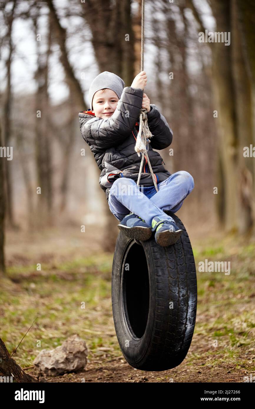 Glückliches Kind schwingt auf einem Autoreifen, der als Schaukel verwendet  wurde Stockfotografie - Alamy