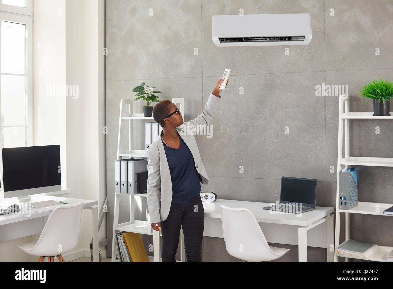 Eine schwarze Frau schaltet mit einer Fernbedienung eine moderne Klimaanlage im Büro um Stockfoto
