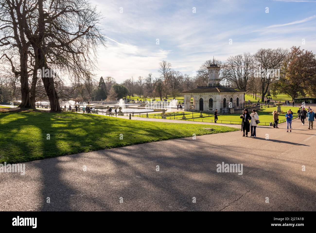 Bäume werfen an einem hellen und sonnigen Wintertag lange Schatten in den Ital Gardens im Hyde Park, London. Stockfoto