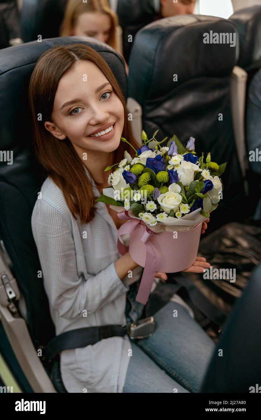 Fröhliche Frau mit Blumen, die mit dem Flugzeug unterwegs ist Stockfoto