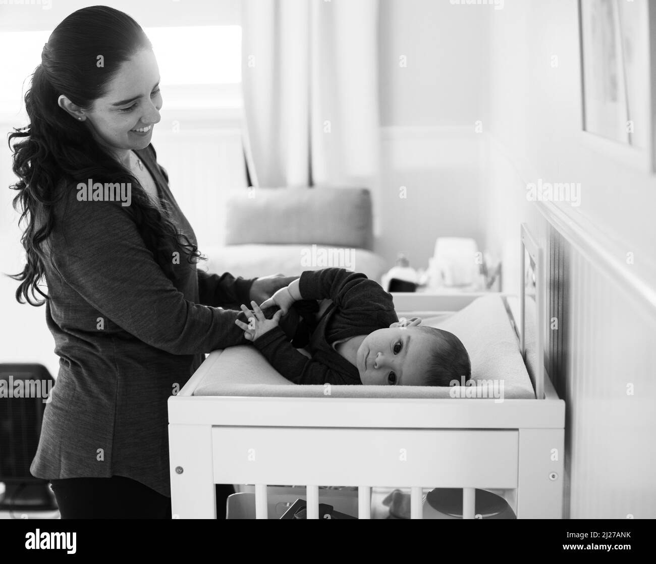 Eine monochrome neue Mutter lächelt ihr Baby in einer sonnenbeschienenen Kinderstube an Stockfoto