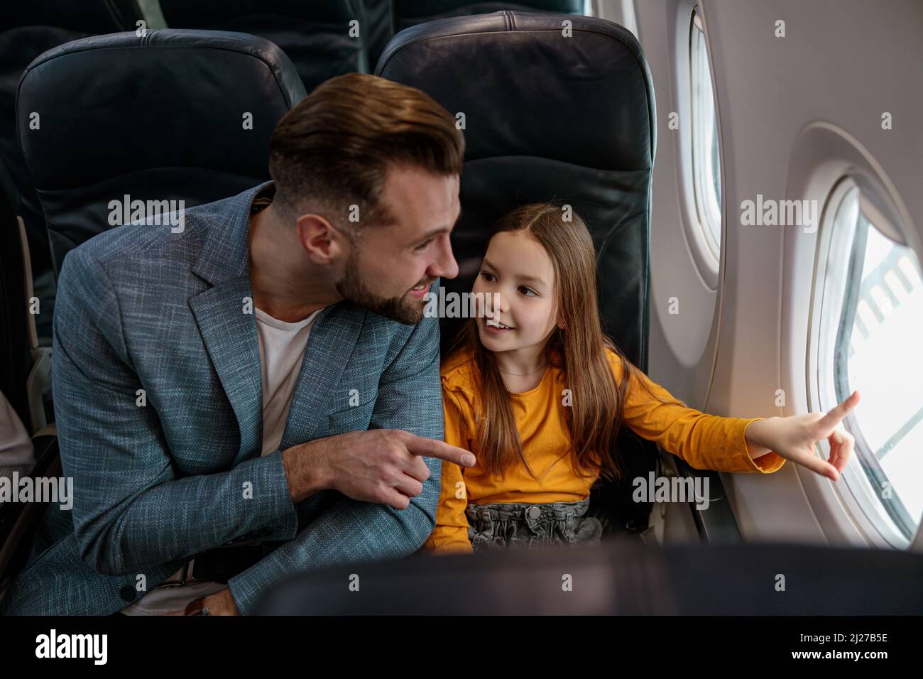 Fröhliches Mädchen und ihr Vater blicken aus dem Fenster im Flugzeug Stockfoto