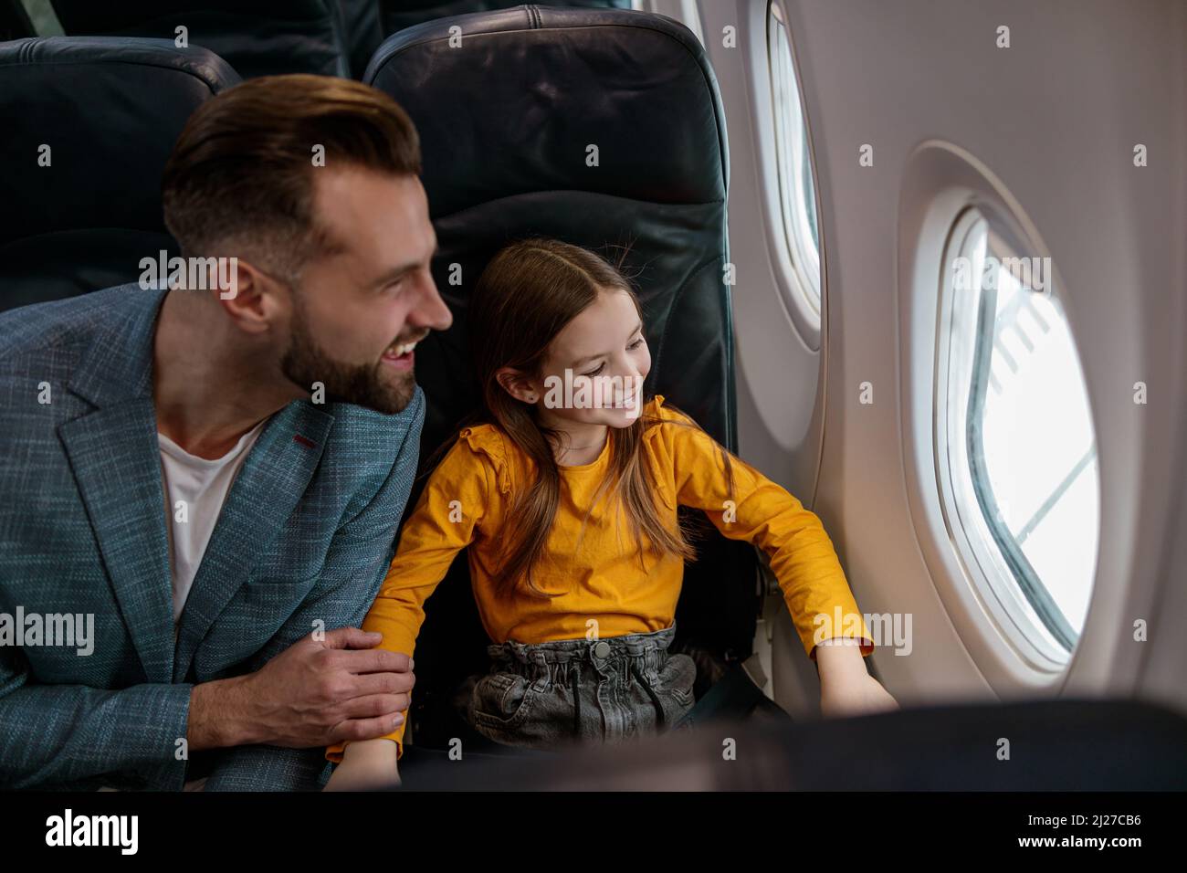 Glücklicher Vater und Tochter, die aus dem Flugzeugfenster schauten Stockfoto