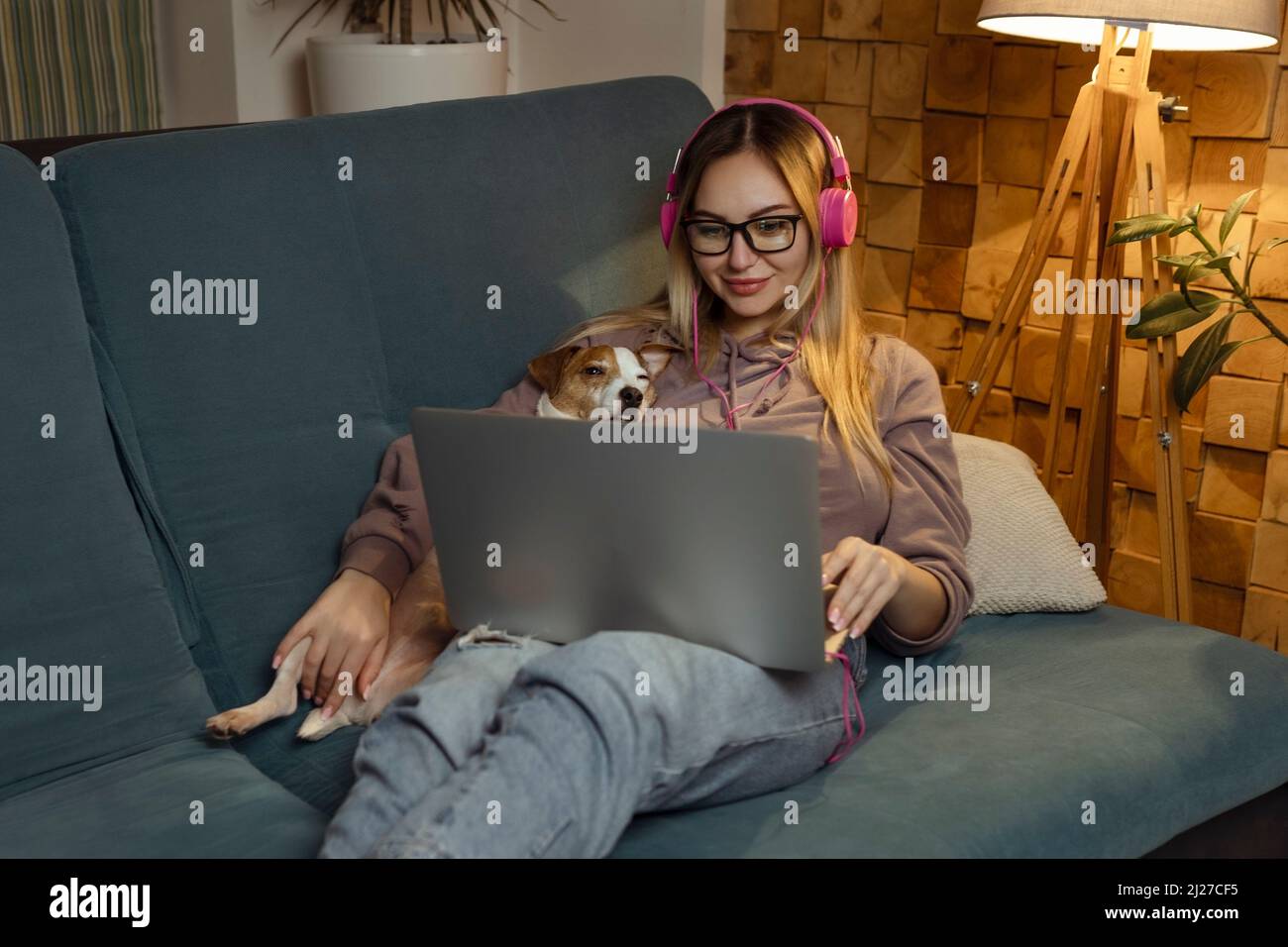 Ein Mädchen mit einem Hund, der einen Film auf einem Laptop mit Kopfhörern ansieht. Haustiere und Freunde für Menschen Stockfoto