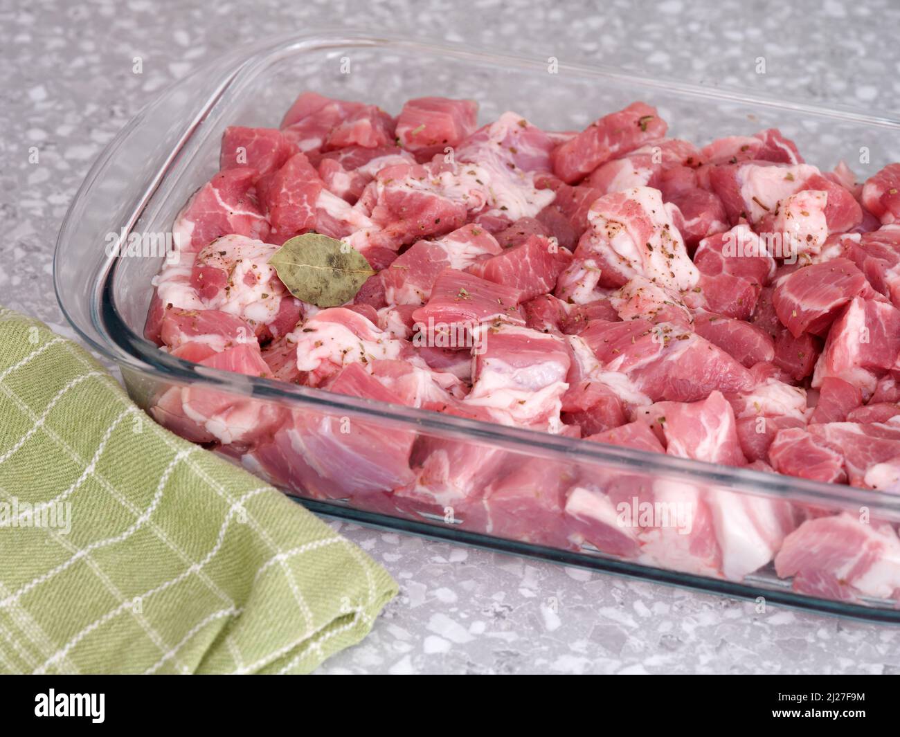 In Scheiben geschnittenes Schweinefleisch mit einem einzelnen Lorbeerblatt auf einem Glasbackblech. Stockfoto