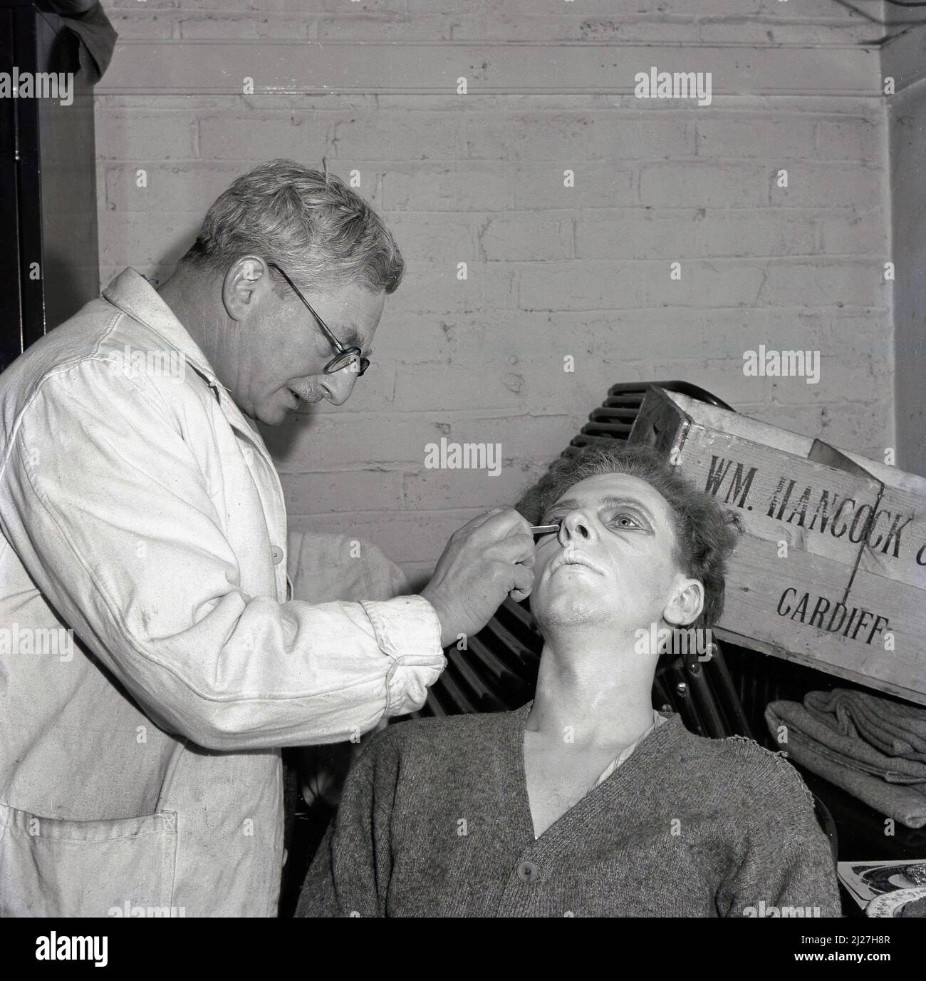 1950s, historisch, ein männlicher Darsteller mit Make-up, Lidschatten vor einer Vorstellung an Mitarbeiter der Steel Company of Wales, Abbey Works, Port Talbot, Wales, Großbritannien. Eine Holzkiste mit den Brauern William Hancock & Co aus Cardiff kann auf einigen Stühlen hinter ihnen ruhen gesehen werden. Stockfoto