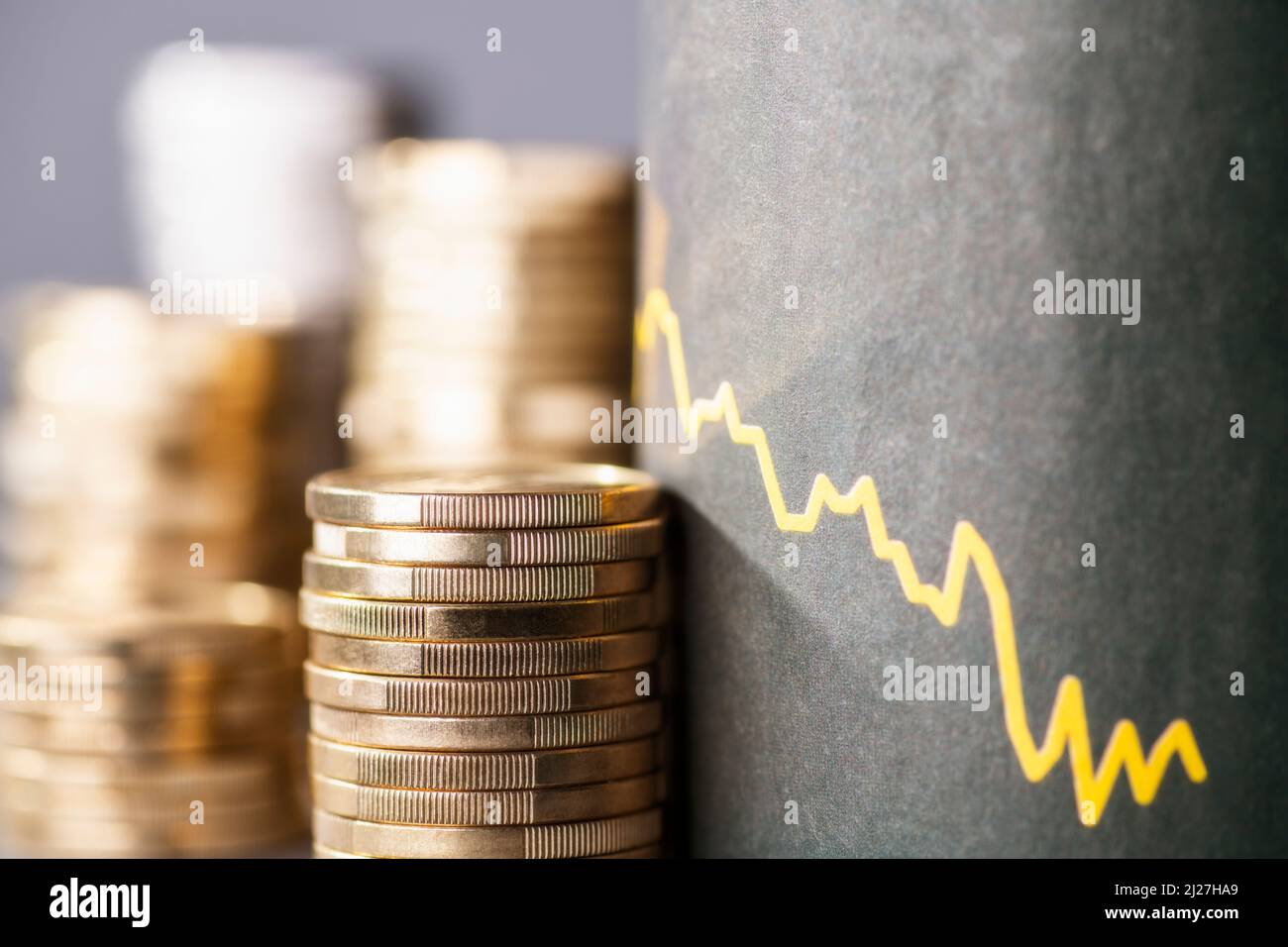 Stapel von Münzen neben einer Abwärtskurve, die den Wertverlust des Geldes durch Inflation symbolisiert Stockfoto