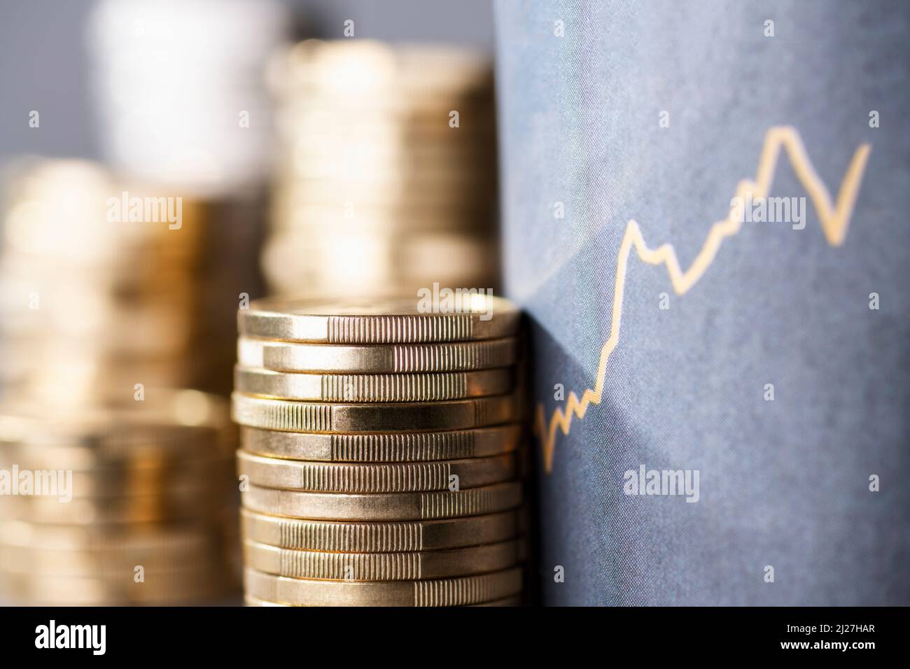 Stapel von Münzen neben einer Aufwärtskurve, die steigende Kosten aufgrund der Inflation symbolisiert Stockfoto