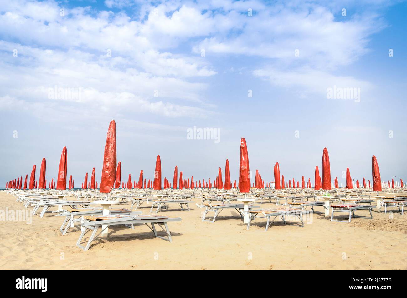 Rote Sonnenschirme und Sonnenliegen am Strand von Rimini - Italienischer Sommerüberblick zu Beginn der Saison Stockfoto