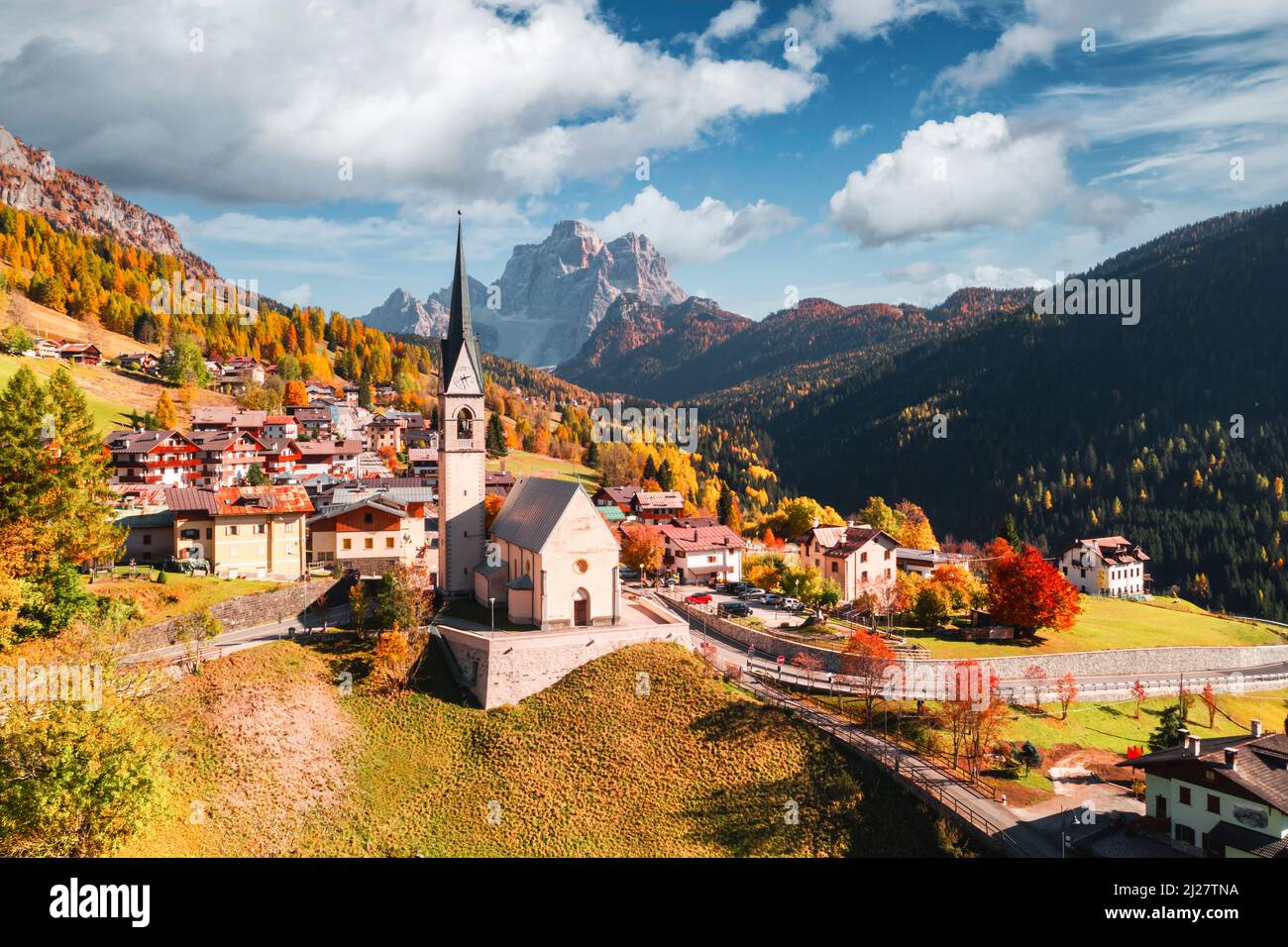 Aerial drone flight over San Lorenzo Catholic church in Selva di Cadore village. Biautiful small city in autumn Dolomites mountains. Dolomite Alps, Province of Belluno, Italy Stockfoto