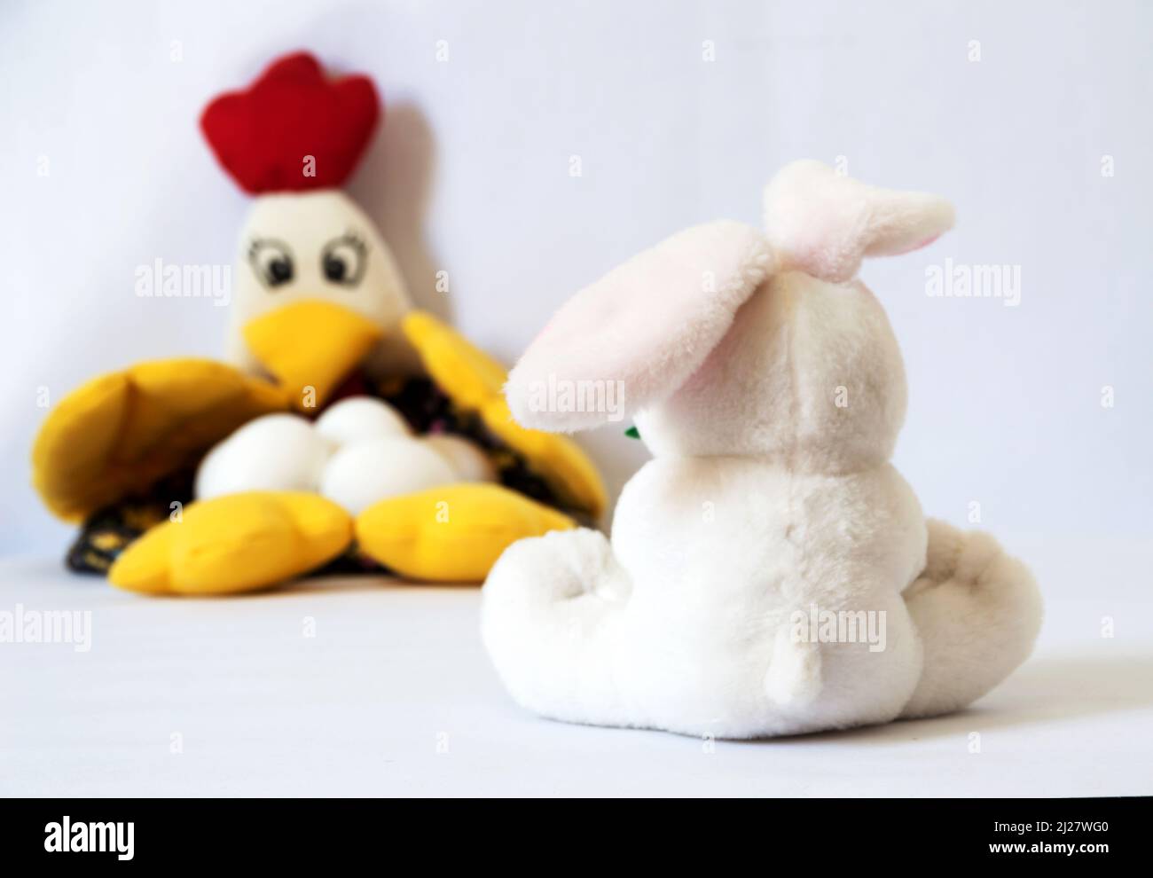 Weißes Plüschhäschen auf dem Rücken mit einem Ohr hinten und einem Ohr nach vorne und Blick auf Huhn mit Eiern, das auf der linken Seite des Fotos unscharf ist Stockfoto