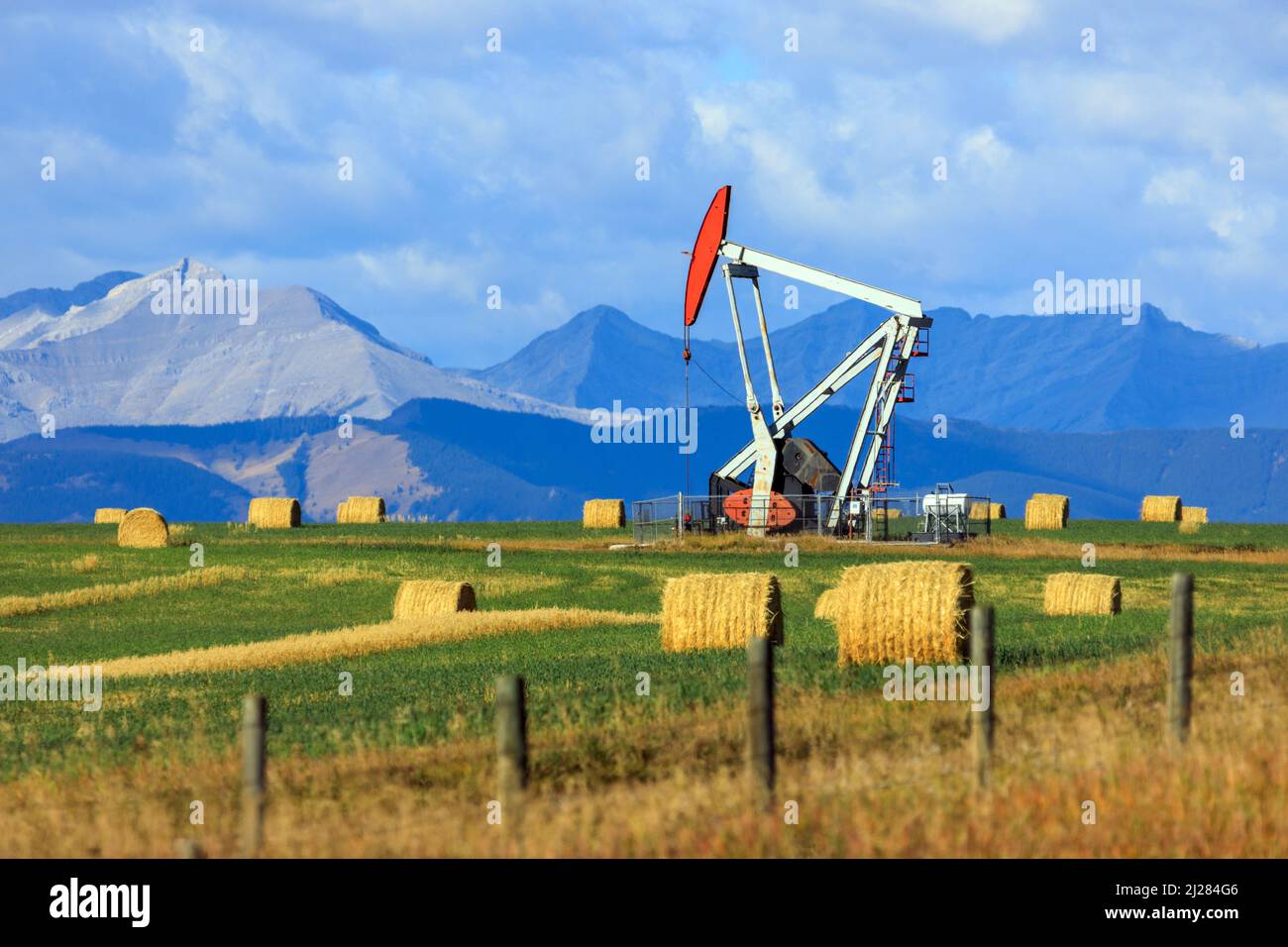 Ein Pumpjack-Bohrgerät der Öl- und Gasindustrie in den kanadischen Prärien mit den kanadischen Rockies in Alberta, Kanada. Stockfoto