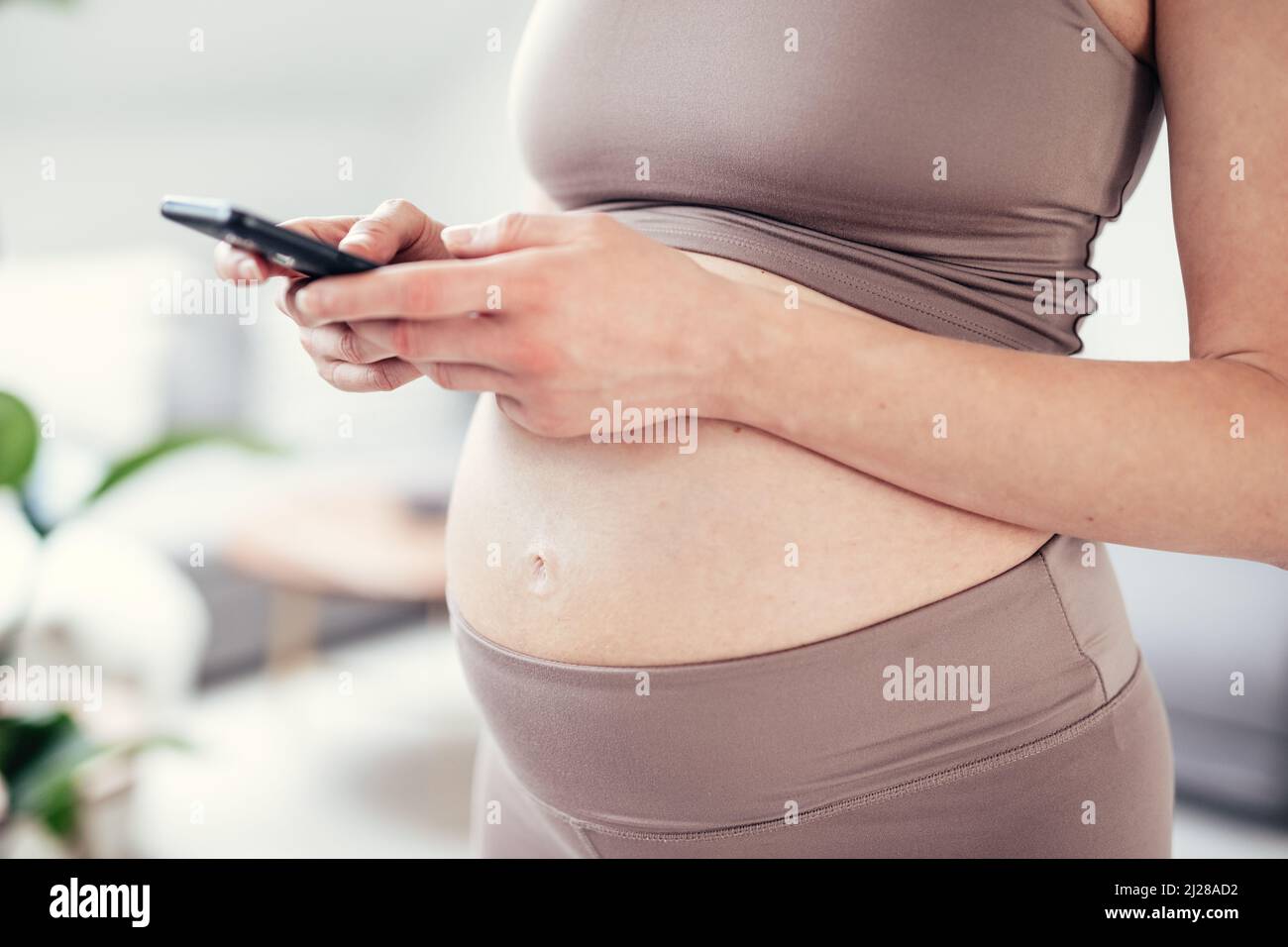 Nahaufnahme des weiblichen Schwangerschaftsbauch. Frau, die die Smartphone-Anwendung in der Wohnung hält und verwendet. Schwangerschaft, Technologie, online Stockfoto