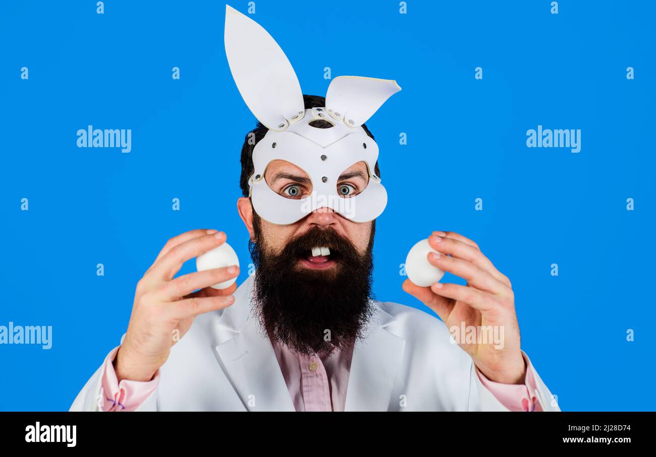 Ostertag. Überraschender bärtiger Mann in Hasenmaske mit zwei weißen Eiern. Bunny Guy. Eiersuche. Stockfoto