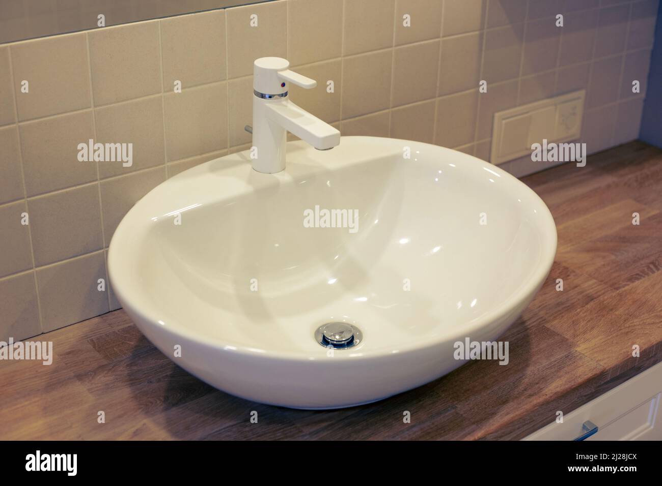 Weißes Waschbecken mit weißem Wasserhahn und hölzerner Arbeitsplatte im Badezimmer Stockfoto