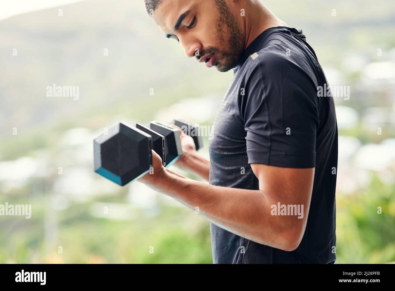 Konzentriert sich auf seine Fitness-Transformation. Eine kurze Aufnahme eines sportlichen jungen Mannes, der Gewichte draußen hebt. Stockfoto