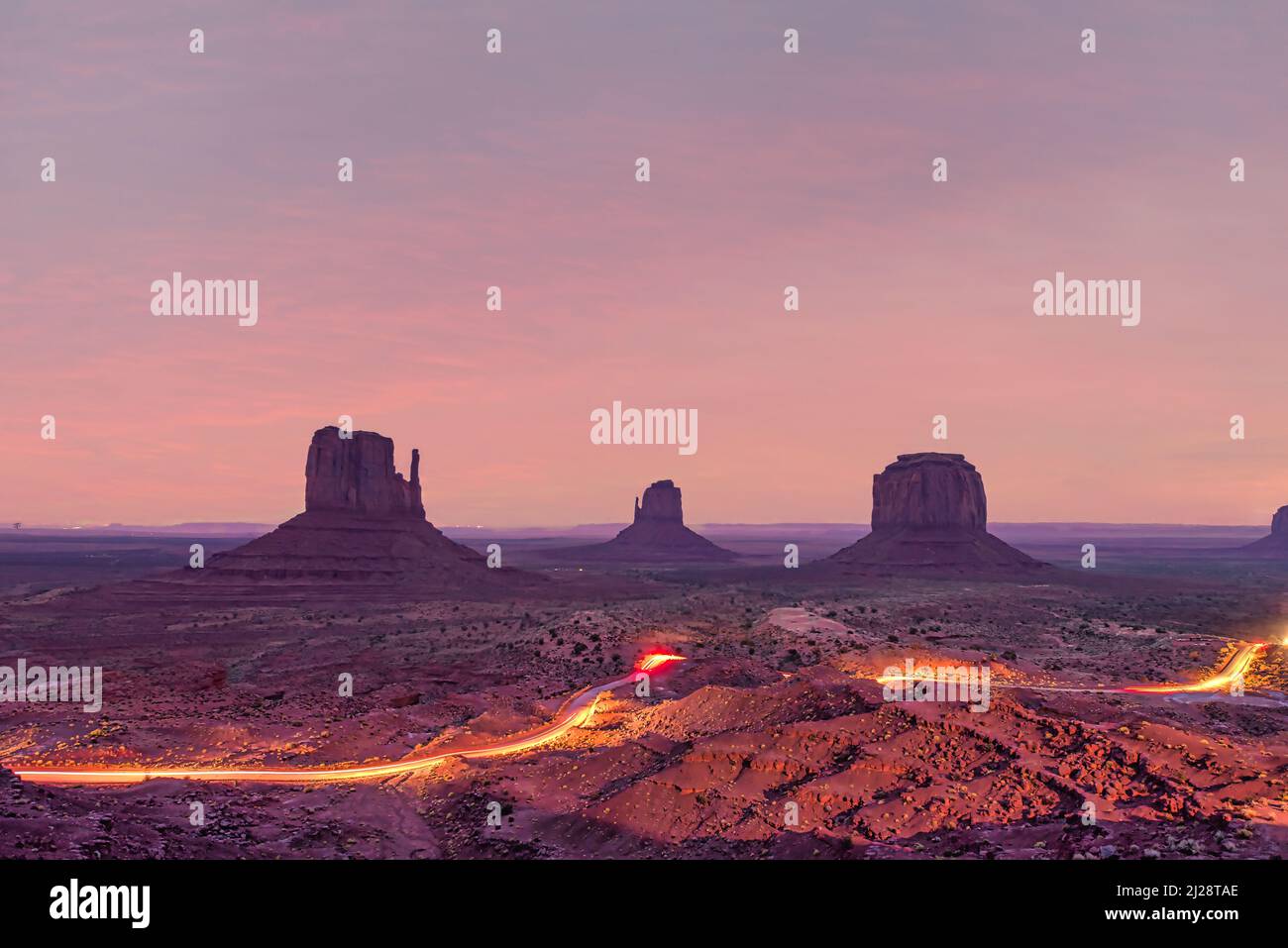 Langzeitbelichtung des Monument Valley bei Nacht mit Autos, die die Schotterstraße der Loop-Tour beleuchten Stockfoto