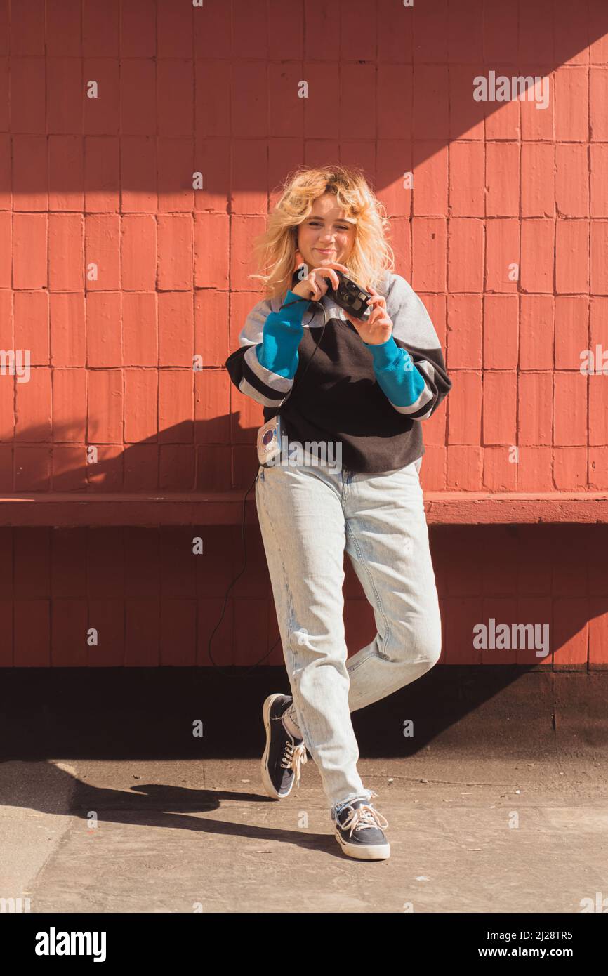 Altmodisches Technologiekonzept. Junger Schöpfer, der mit einer alten 90s-inspirierten Analogkamera über einer Backsteinwand fotografiert. Vertikale Aufnahme. Hochwertige Fotos Stockfoto