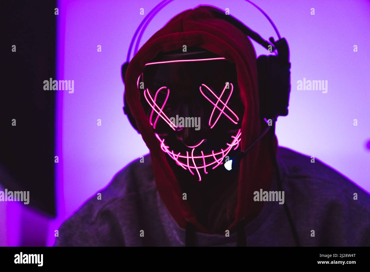 Maskierter anonymer Programmierer, der Kopfhörer und einen Hoodie trägt. Rosa Hintergrund. Hochwertige Fotos Stockfoto