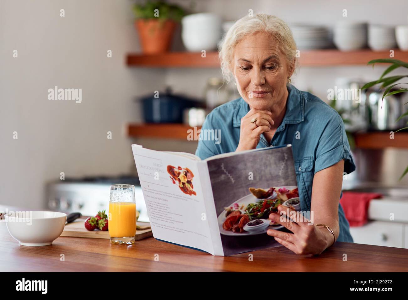 Der gesunde Weg ist der kluge Weg. Aufnahme einer reifen Frau, die ein Buch liest, während sie das Frühstück zu Hause vorbereitet. Stockfoto