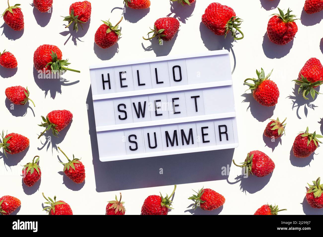 Hello Sweet Summer Text auf Leuchtkasten und Erdbeere auf weißem Hintergrund. Kreatives Konzept Sommerzeit. Draufsicht, Flat Lay, Grußkarte. Stockfoto