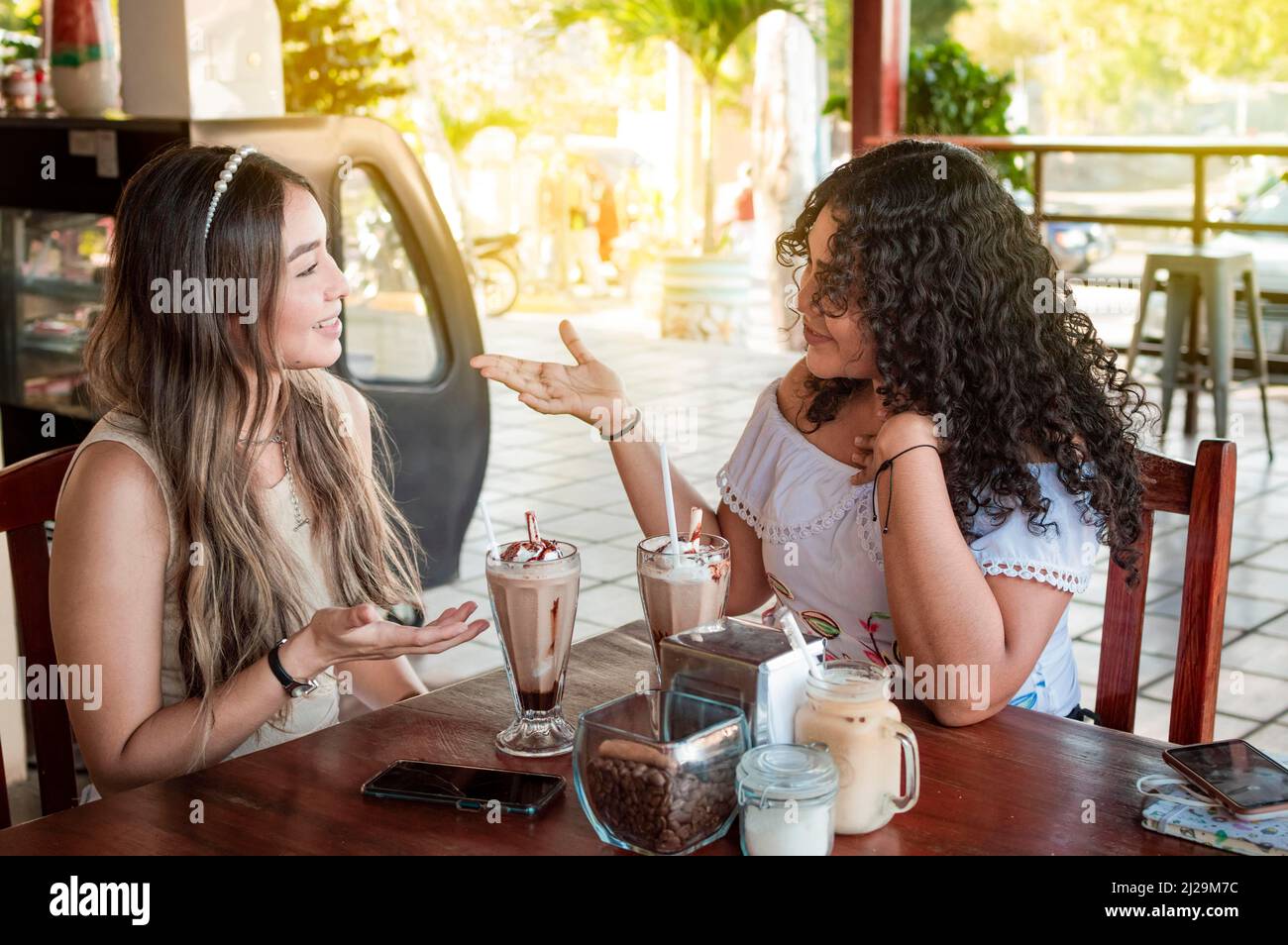 Zwei niedliche Mädchen, die in einem Café ein Gespräch führen, zwei Freundinnen, die in einem Café über Ideen diskutieren Stockfoto