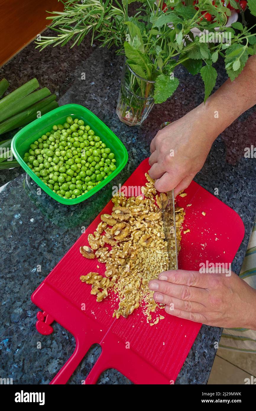 Süddeutsche Küche, Backen, herzhafte Gemüsekuchen mit Walnussbasis zubereiten, Walnüsse mit Messer hacken, Hacken, rotes Schneidebrett, Herrengerichte Stockfoto