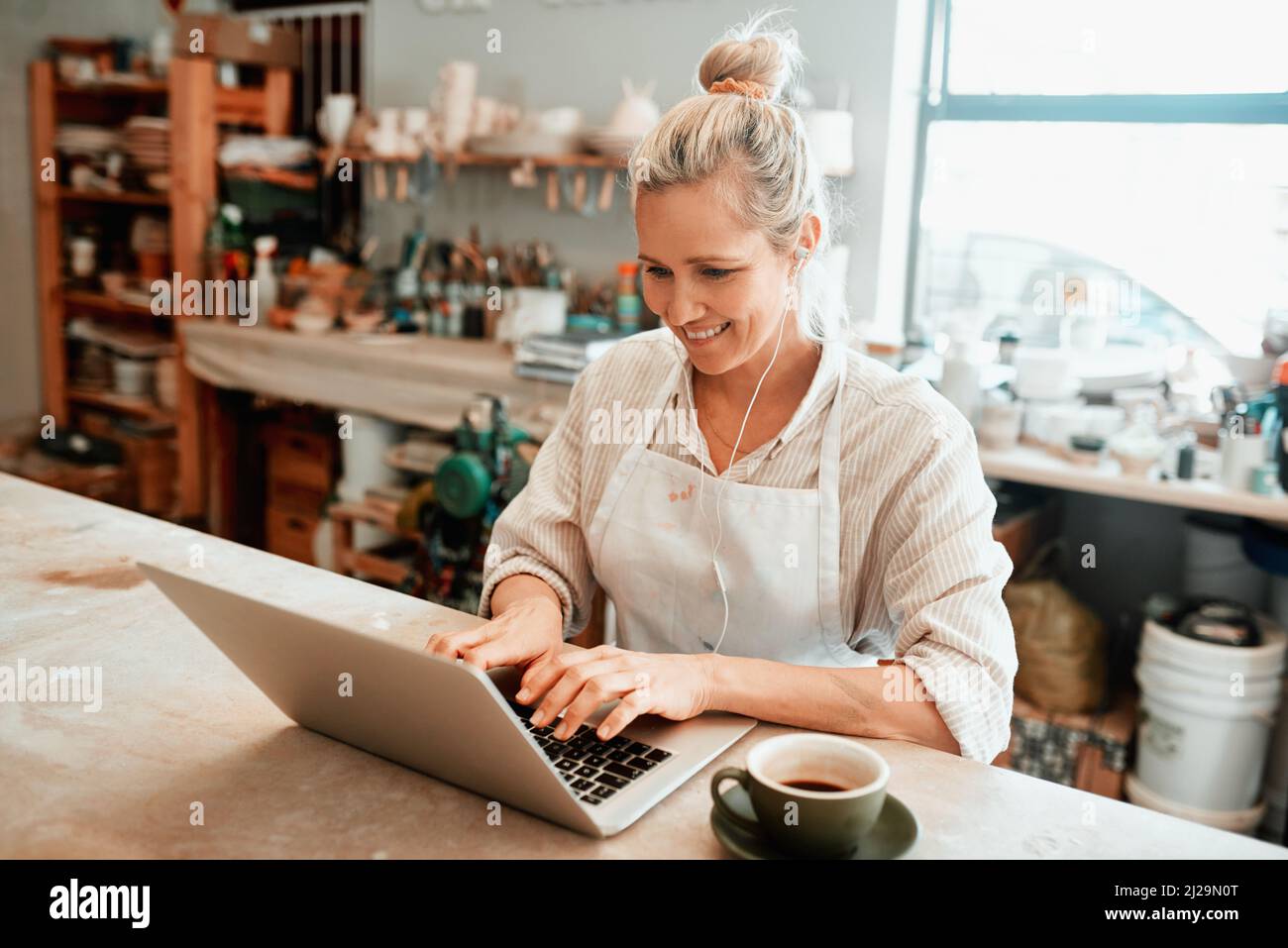 Ich versuche, mit meinen Online-Verkäufen Schritt zu halten. Ausgeschnittene Aufnahme einer Kunsthandwerkerin mit einem Laptop in ihrer Werkstatt. Stockfoto